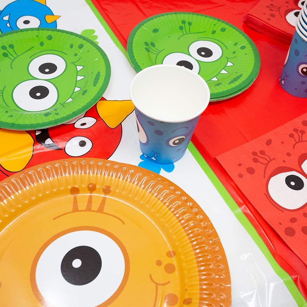 Image of a table set up for a Monster-themed party, featuring monster-themed paper dinner plates, dessert plates, and lunch napkins. The table is covered with plastic table covers in red and white.